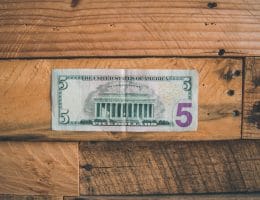An all American $5 bill sitting on a wooden table.