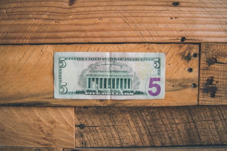 An all American $5 bill sitting on a wooden table.