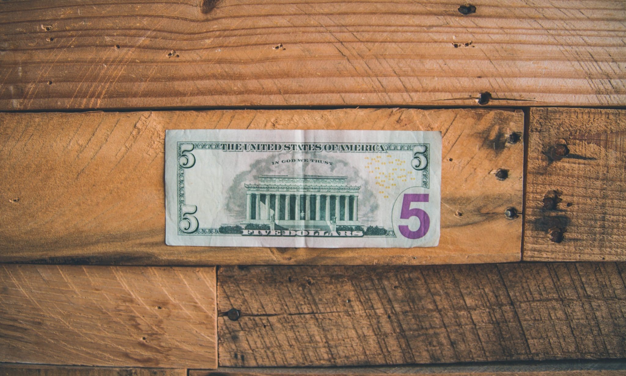 An all American $5 bill sitting on a wooden table.