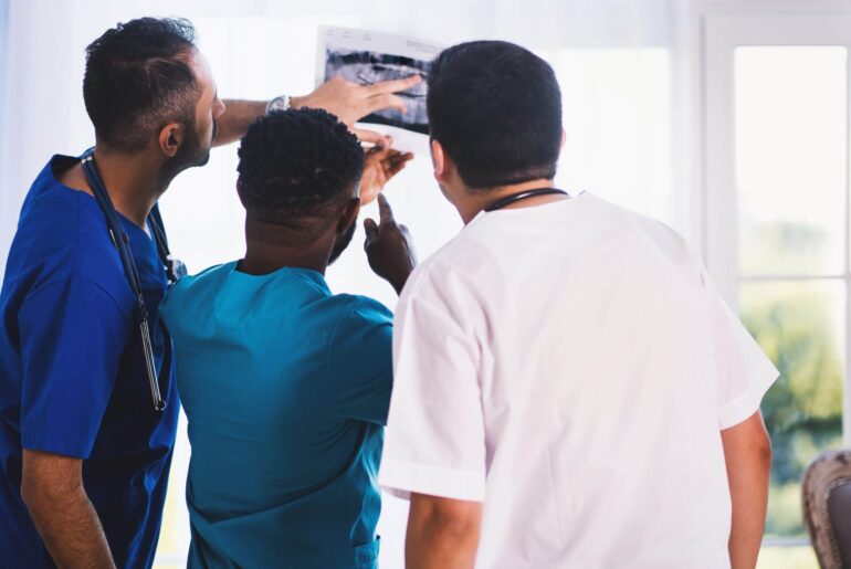 Three doctors examine an x-ray and seem to be very interested