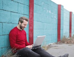 A pleasantly bearded man in a red sweater works on his online courses outside.