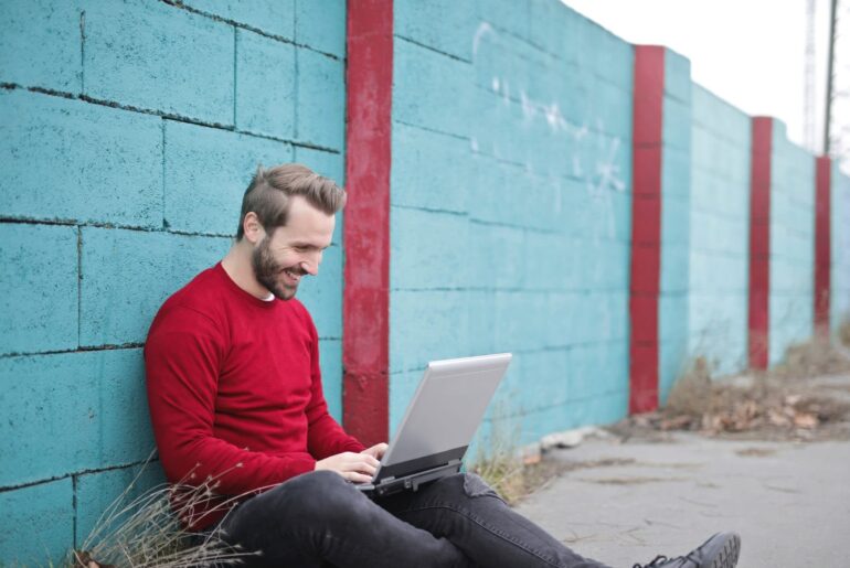 A pleasantly bearded man in a red sweater works on his online courses outside.