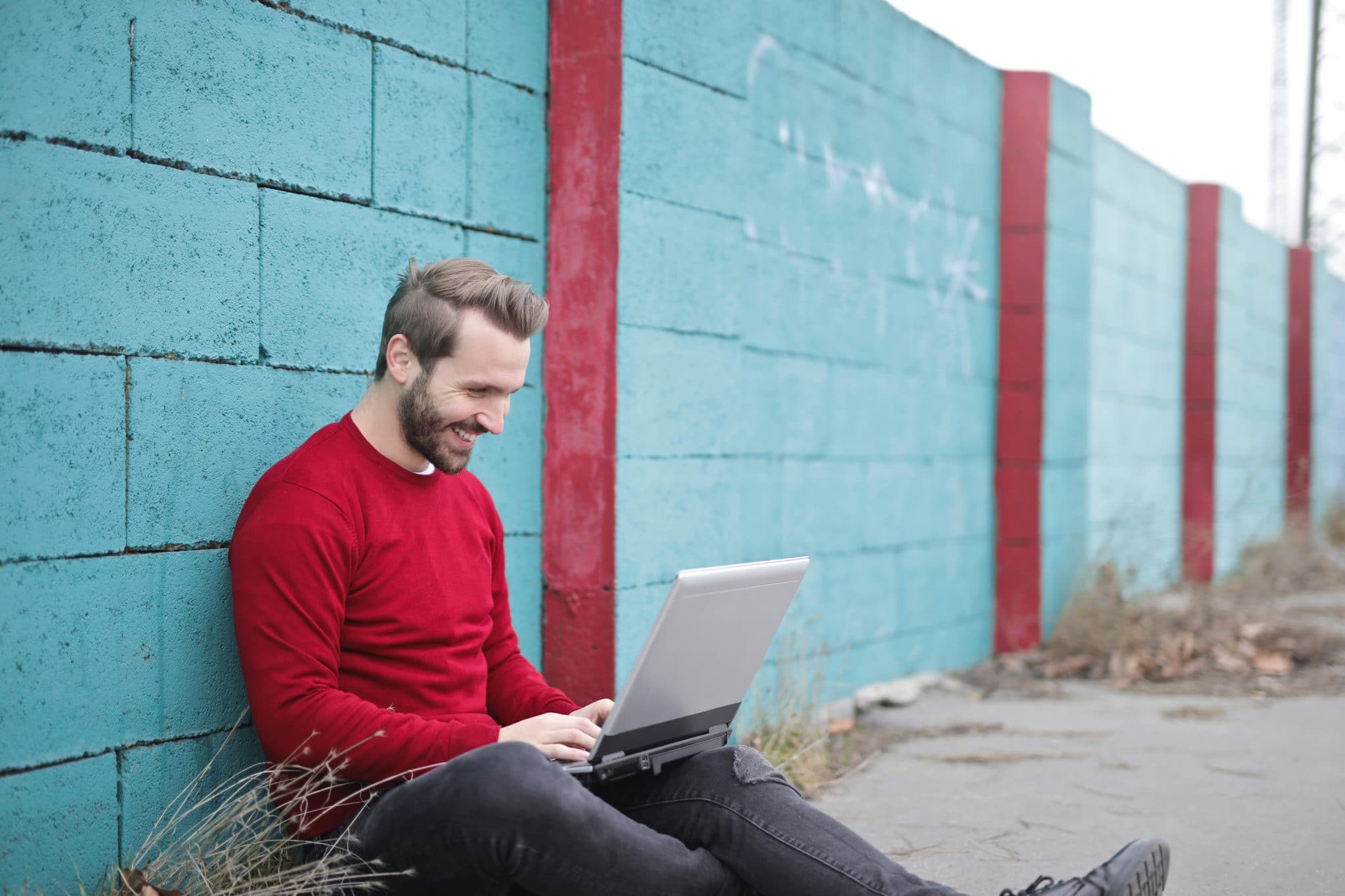 A pleasantly bearded man in a red sweater works on his online courses outside.