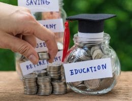 Woman hand holding stack of coins money and glass jar with full of coins and graduates hat label as Education, education or savings concept.
