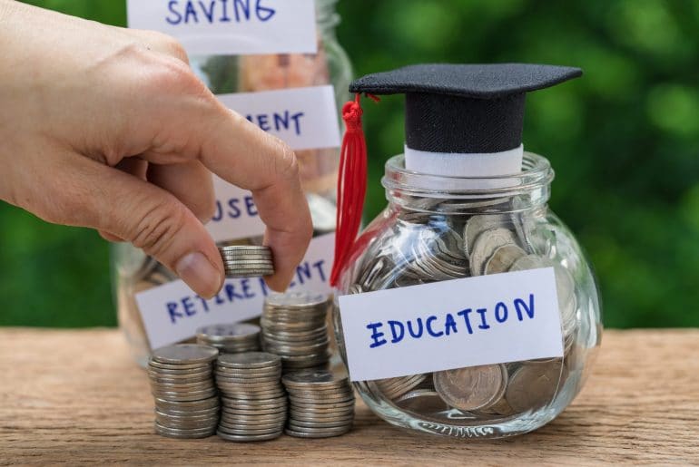 Woman hand holding stack of coins money and glass jar with full of coins and graduates hat label as Education, education or savings concept.