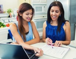 Mother and teenage daughter are in the kitchen researching colleges and filling out university applications.