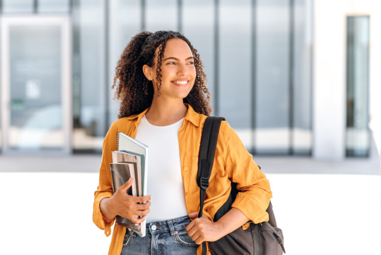 Student with backpack and books looking of into the distance with hope imagining her back-to-school success and being highly motivated.