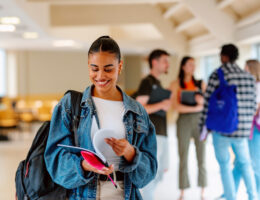 Student looking at their text books getting ready to craft an ACT study plan. Other students in the background chatting.