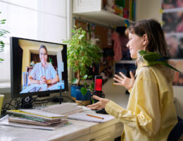 A female presenting student making the most of their online tutoring sessions in their room with their pet parrot on their shoulder.