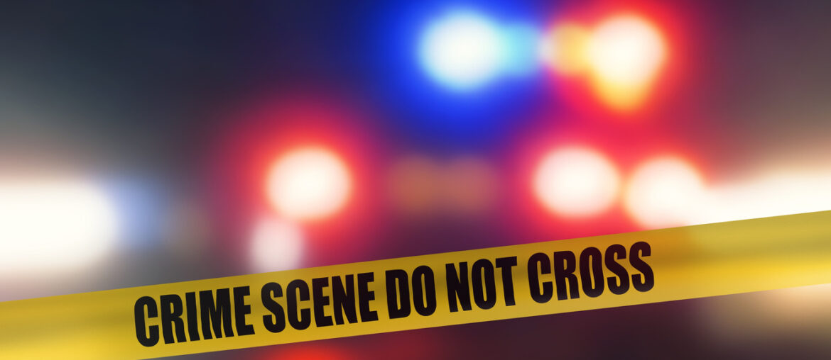 Looking at a tape that says, "crime scene do not cross" with flashing police lights in the background as an ATF Special Agent